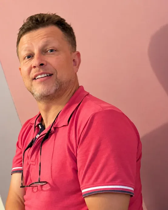 Czarek w różowej koszulce polo, uśmiechnięty, na tle różowej ściany